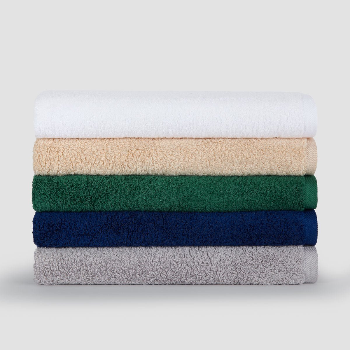 Pilha de cinco toalhas de bambu dobradas em branco, bege, verde, azul-marinho e cinzento exibidas contra um fundo claro.