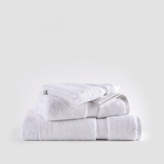 Conjunto de toalhas de bambu branco empilhadas mostrando toalhas de rosto, mão e banho com fitas texturadas em fundo neutro.