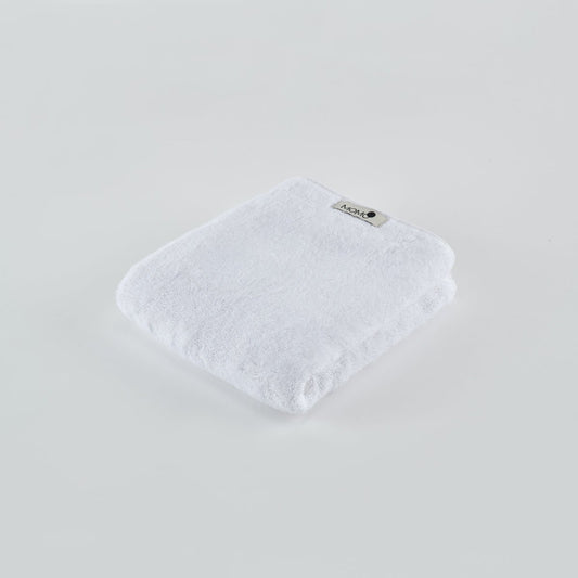 Toalha de bambu branca Momo Cotton dobrada em fundo claro com etiqueta de marca visível