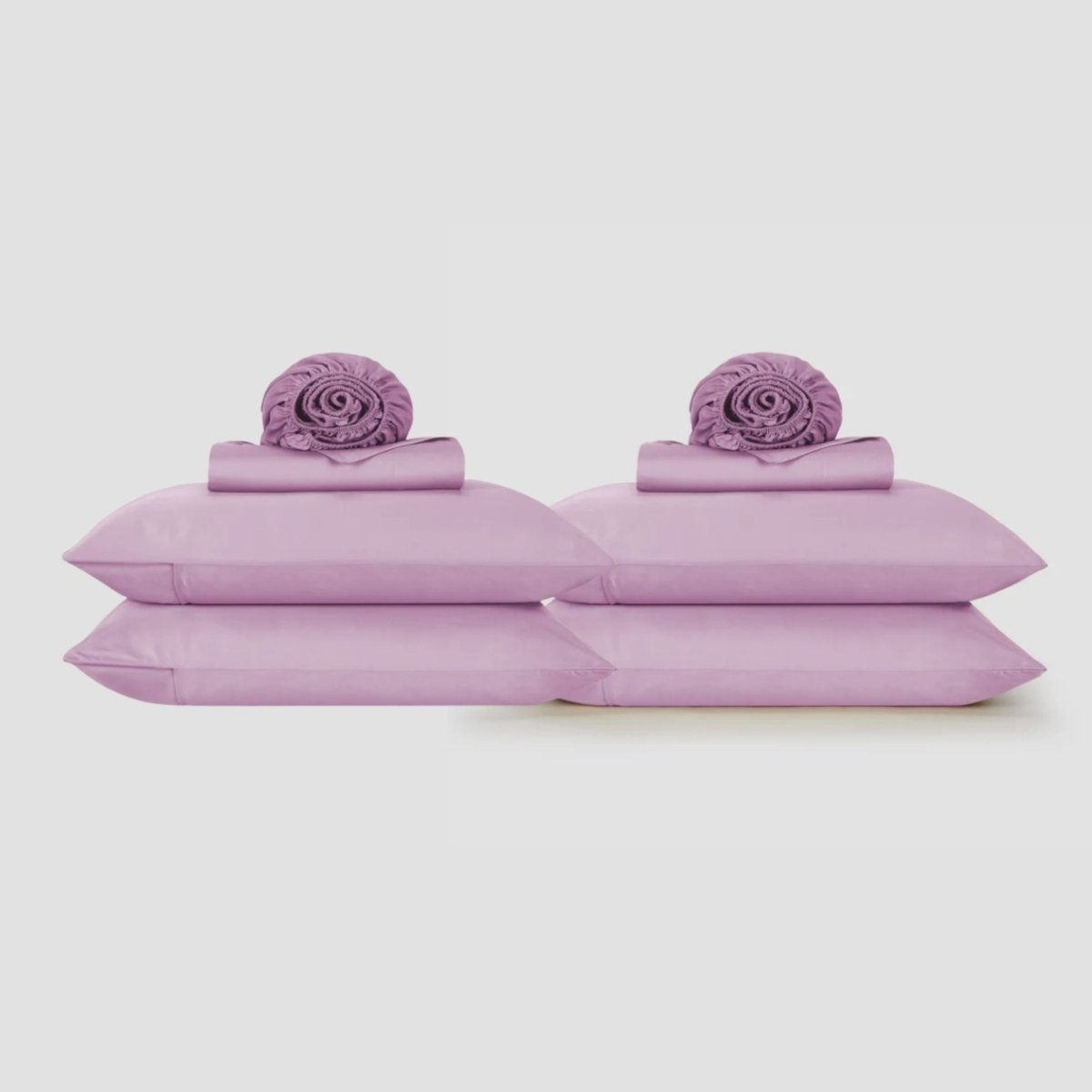 Lençol roxo lavanda apresentado em plano com fronhas correspondentes e elementos decorativos enrolados em fundo neutro