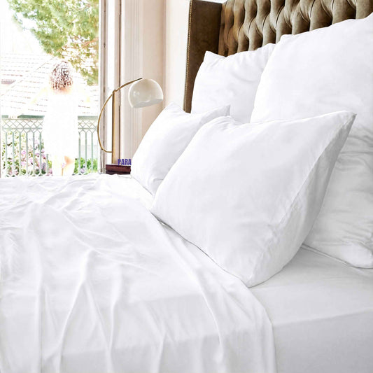 Jogo lençol de cima branco em cama com almofadas e cabeceira estofada, junto a janela com vista para varanda