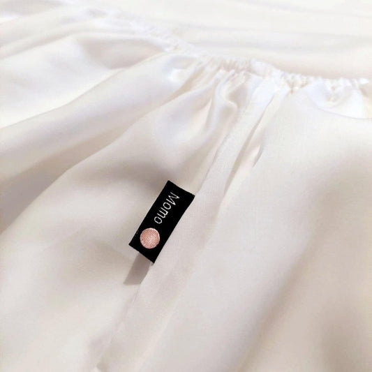 Lençol ajustado branco de bambu com etiqueta da marca momo-cotton na superfície do tecido dobrado