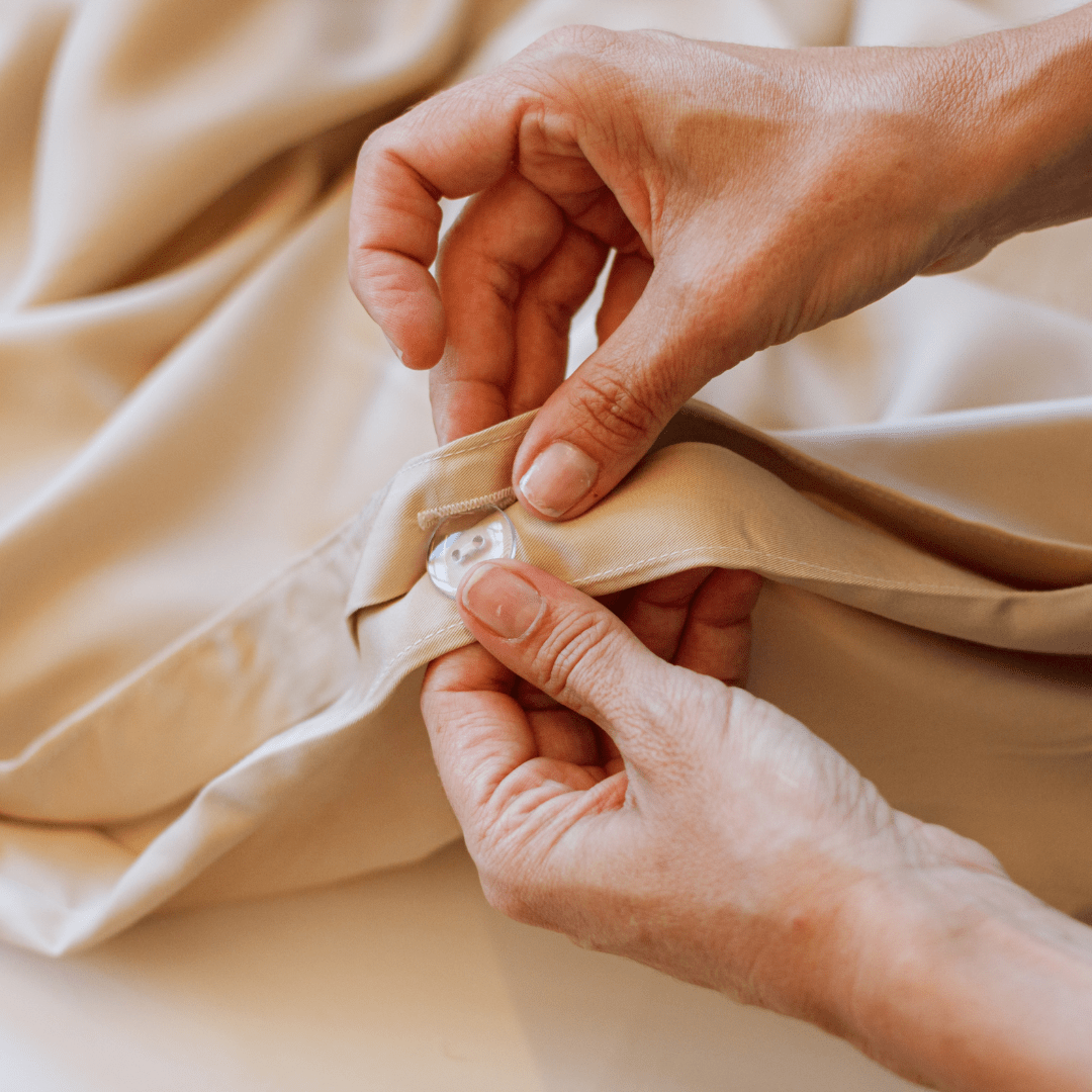Mãos tocando roupa de cama e toalhas de algodão bege macio do conjunto de lençol completo Momo Cotton