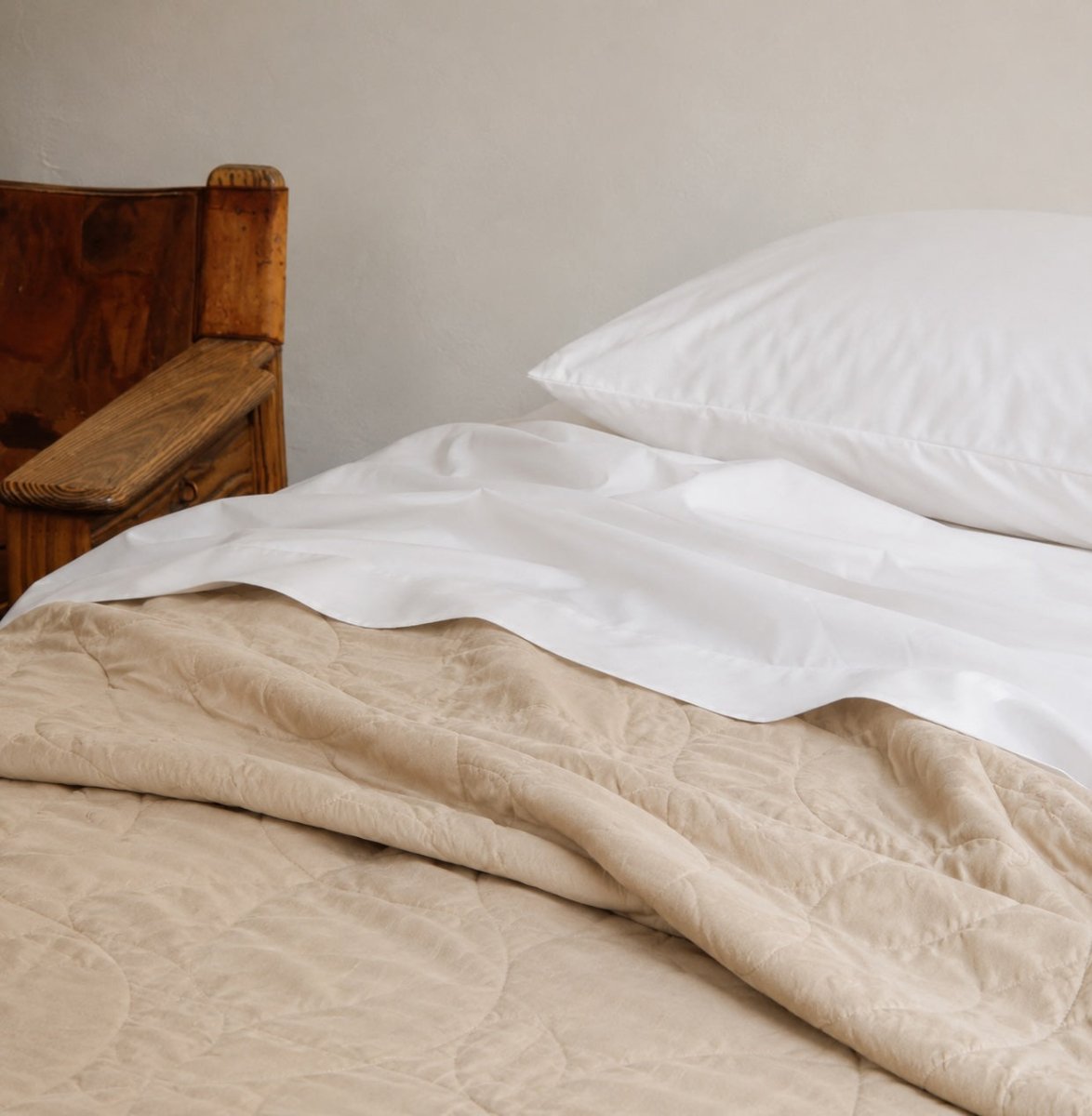 Colcha de verão acolchoada bege em camada sobre lençol branco com almofadas em cama de madeira