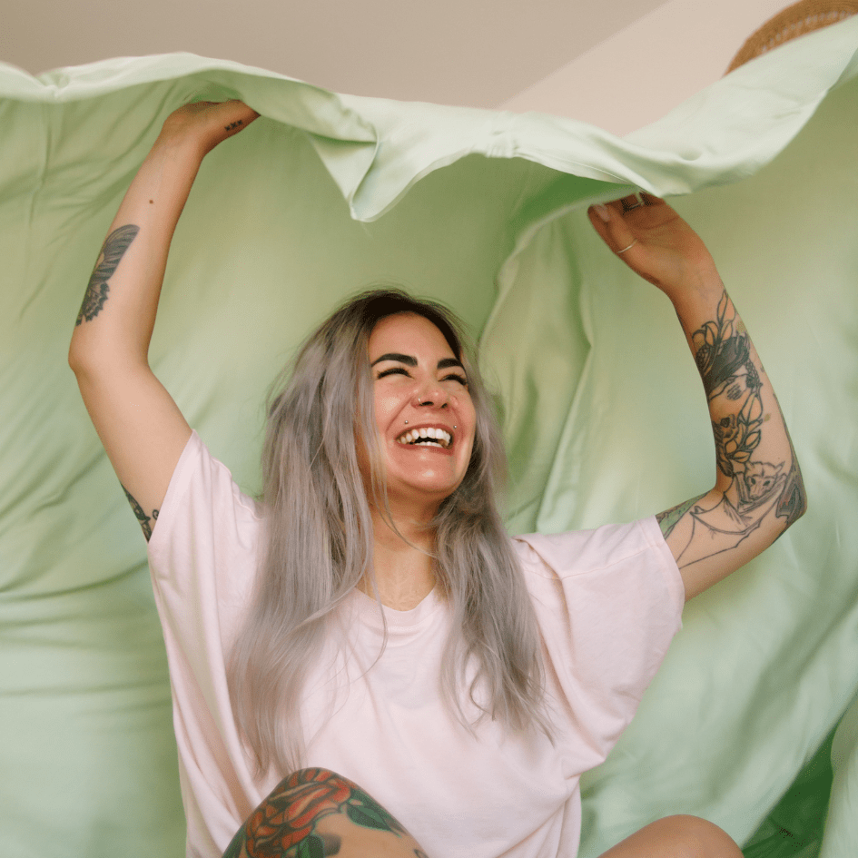 Mulher sorridente a segurar roupa de cama verde e branca para noites de verão confortáveis