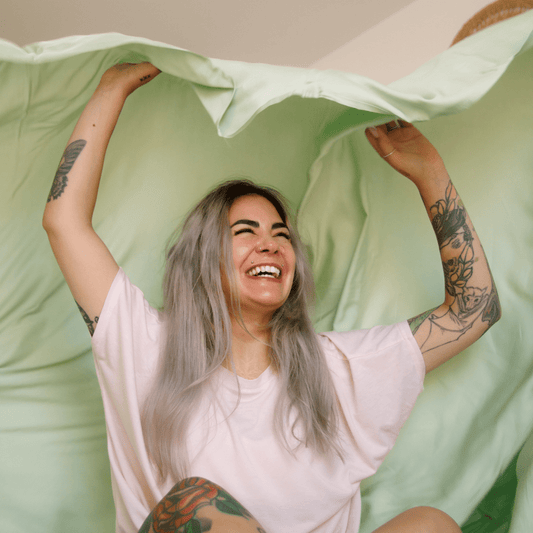Mulher sorridente a segurar roupa de cama verde e branca para noites de verão confortáveis