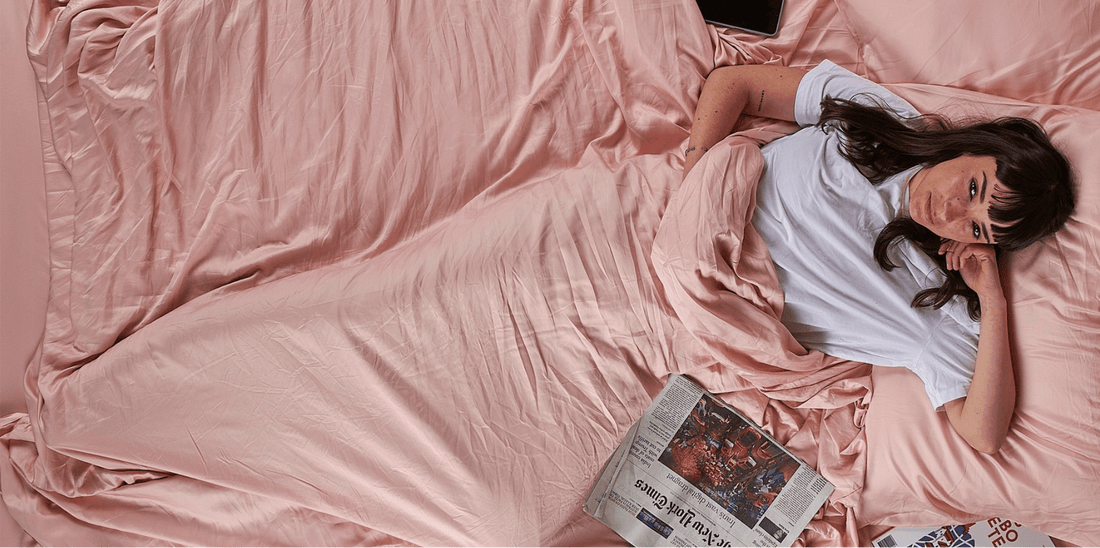 Rapariga deitada numa cama com roupa de cama rosa a ler jornal, decoração de quarto primavera.