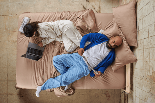 Casal na cama com lençóis de bambu durante o dia, mostrando conforto em diferentes estações do ano.