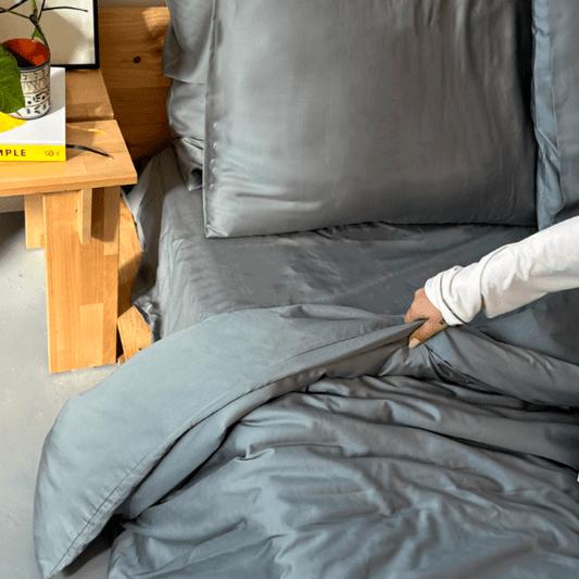 Mulher tocando roupa de cama de bambu cinzenta em cama com mesa de madeira ao fundo