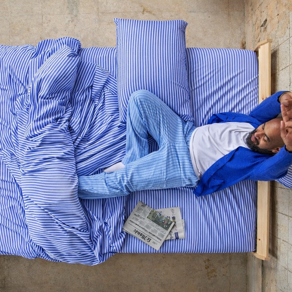 Homem a dormir confortavelmente em lençóis de bambu azuis e brancos listrados.
