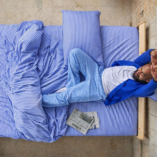 Homem a dormir confortavelmente em lençóis de bambu azuis e brancos listrados.