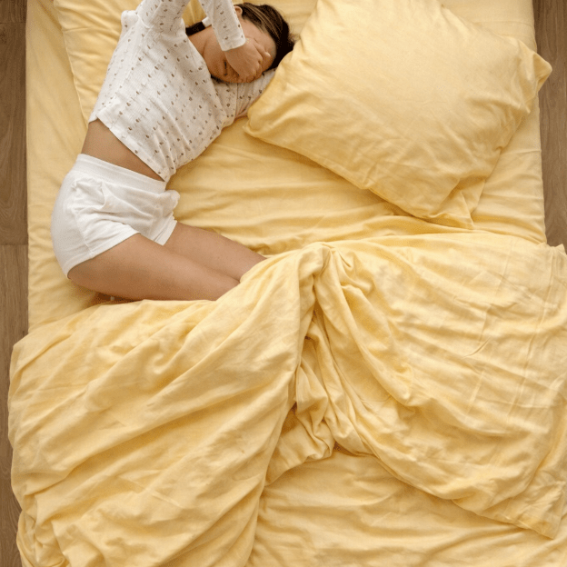 Bed with yellow bedding and pillow, person lying in a decorative bedscaping pose.
