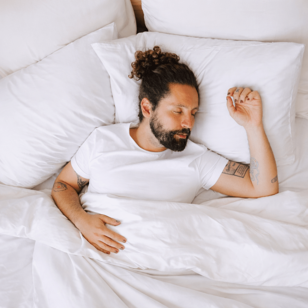 Homem a dormir confortavelmente em lençóis de bambu brancos e hipoalergénicos