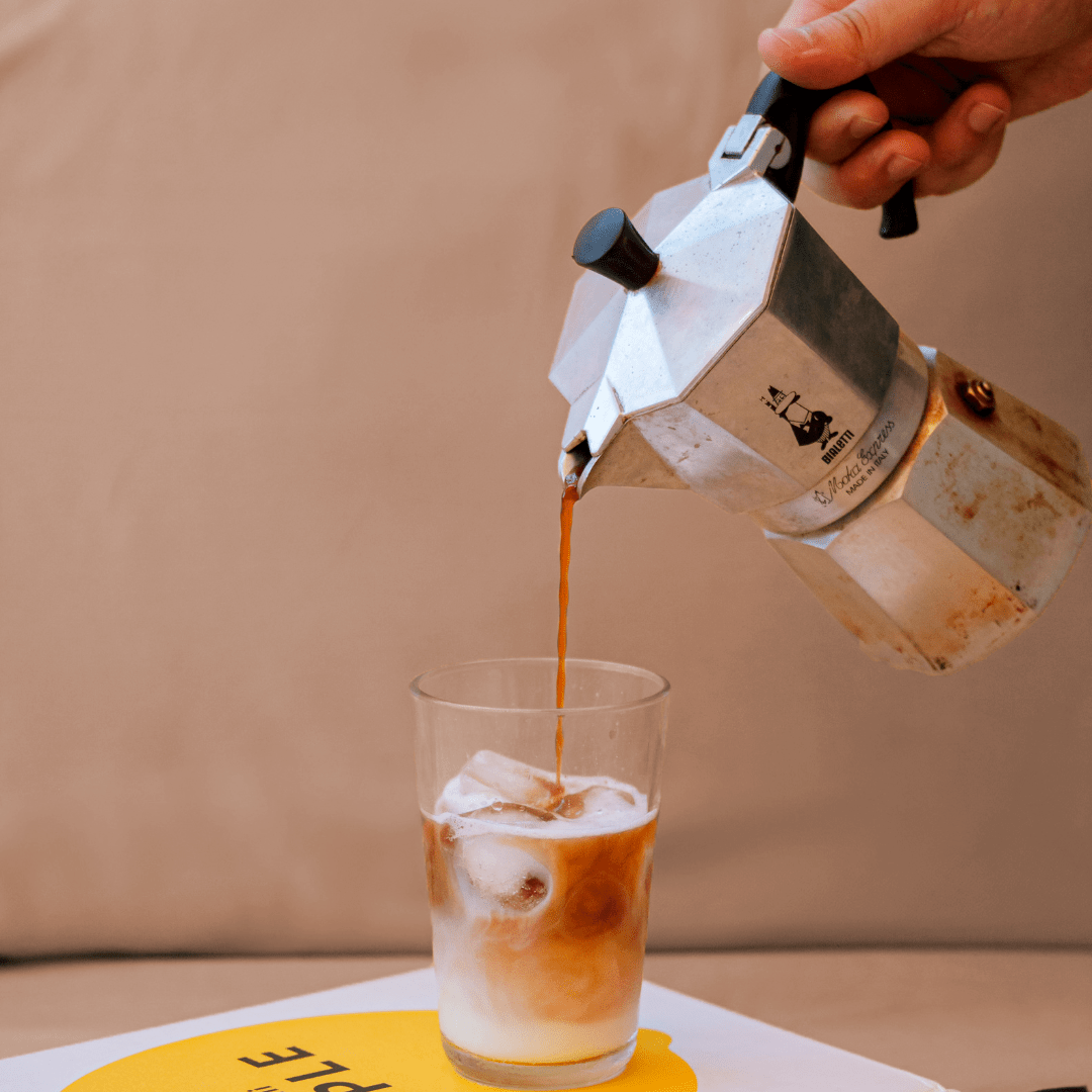 Moka quente a ser despejada numa chávena com gelo sobre fundo bege.