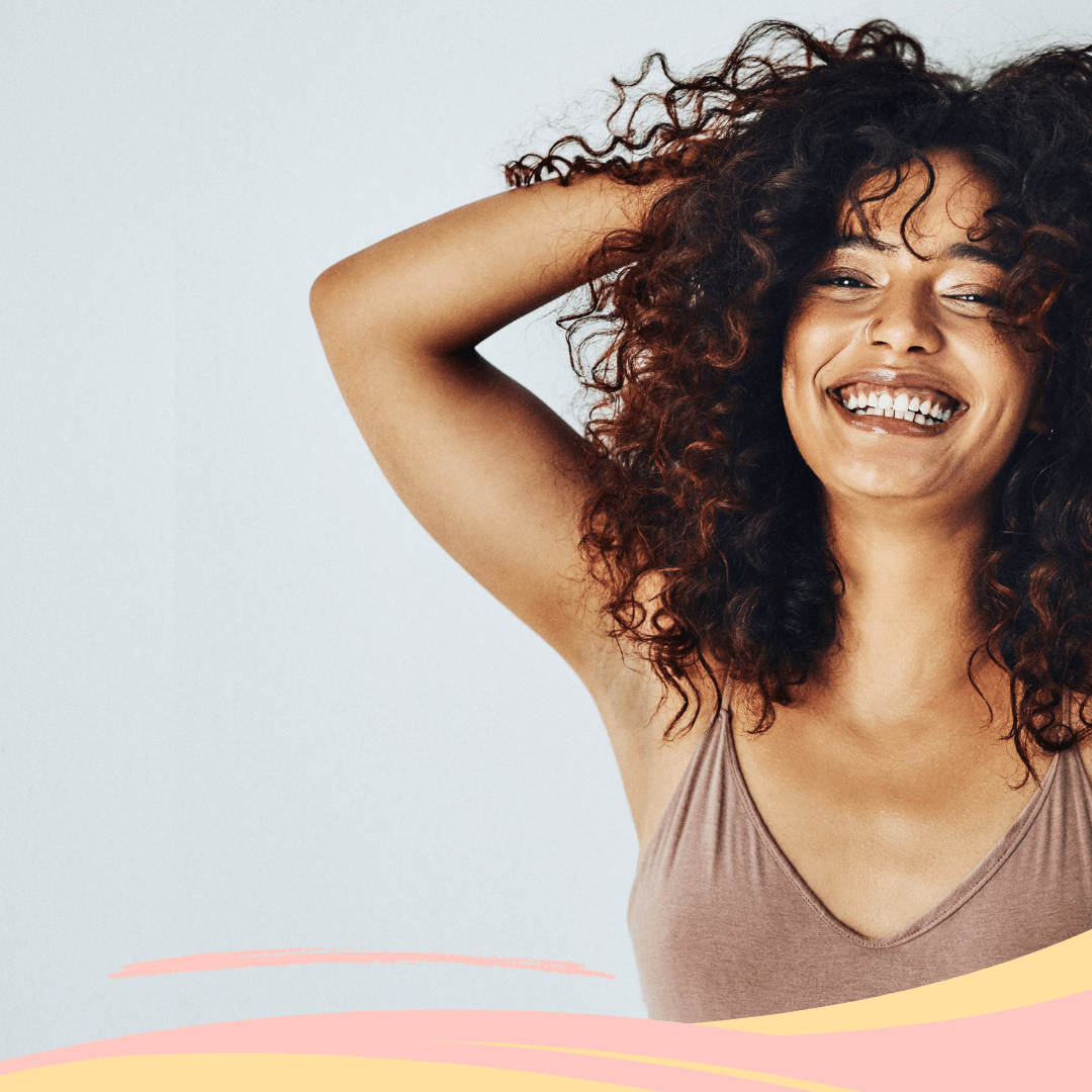 Woman with brown curly hair smiling, displaying hydrated and healthy hair.