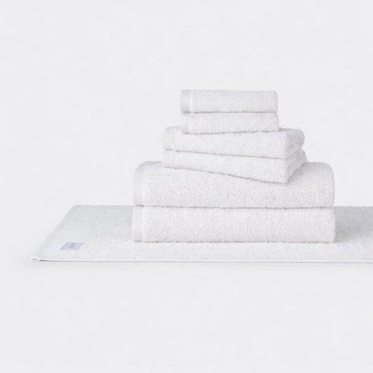 Stack of white Wabi Sabi cotton towels arranged by size on a light background