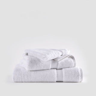 Conjunto de toalhas de bambu branco empilhadas mostrando toalhas de rosto, mão e banho com fitas texturadas em fundo neutro.