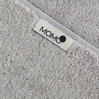 Toalha de bambu cinzenta com etiqueta da marca momo-cotton em acabamento branco, close-up da textura macia