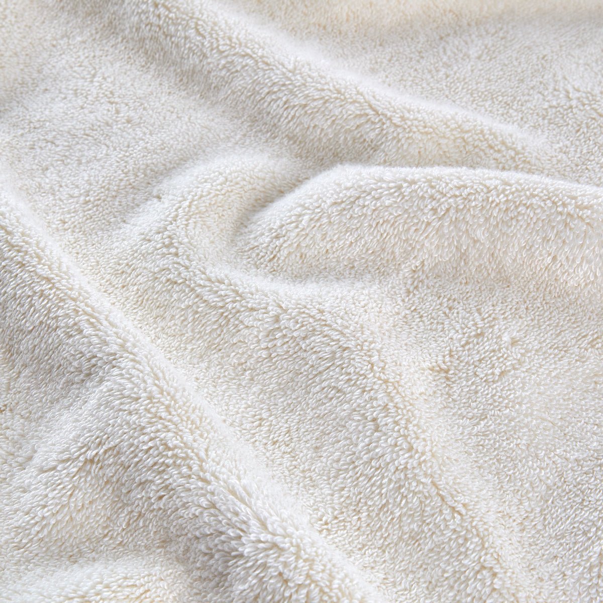 Conjunto de toalhas de bambu cor creme dobradas e empilhadas, mostrando textura macia e detalhe de fibras naturais