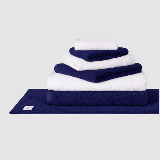 Conjunto de toalhas Wabi Sabi azul-marinho e branco empilhadas em tapete de banho azul-marinho sobre fundo neutro