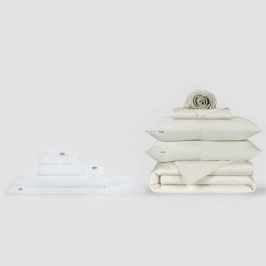 Conjunto de cama Momo Cotton completo e coleção de toalhas apresentados em creme, mostrando roupa de cama e toalhas dobradas em fundo branco