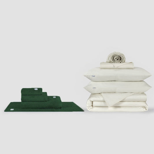 Conjunto de toalhas verdes e lençol branco expostos em fundo neutro pela Momo Cotton