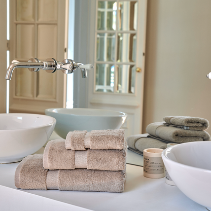 Conjunto de toalhas de bambu Alba empilhadas no lavatório de uma casa de banho elegante, com pia e torneira de design moderno