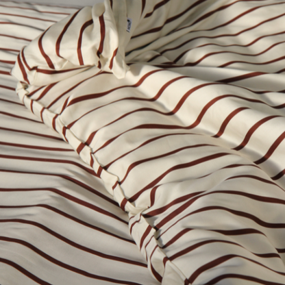 Jogo capa de edredão em bambu com padrão de riscas vermelho e branco, apresentado na cama.