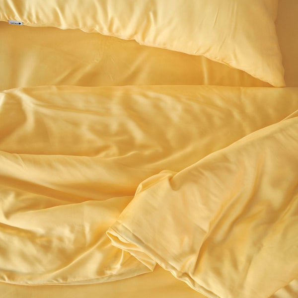 Jogo de cama em bambu creme com almofadas e edredão dobrados, mostrando textura macia do tecido e trama de qualidade