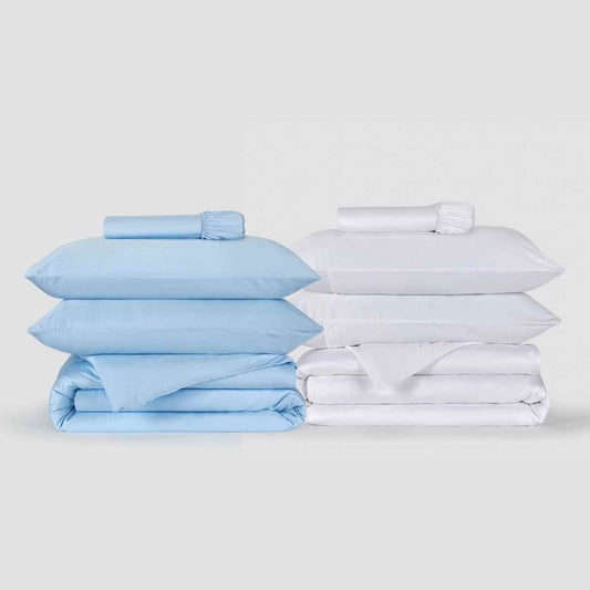 Dois conjuntos de capa de edredão exibidos lado a lado, um azul claro e outro branco, com fronhas e lençóis ajustados combinando