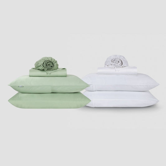 Dois conjuntos de lençóis Momo em algodão lado a lado, um em verde sálvia e outro em branco, cada um empilhado com roupas de cama dobradas