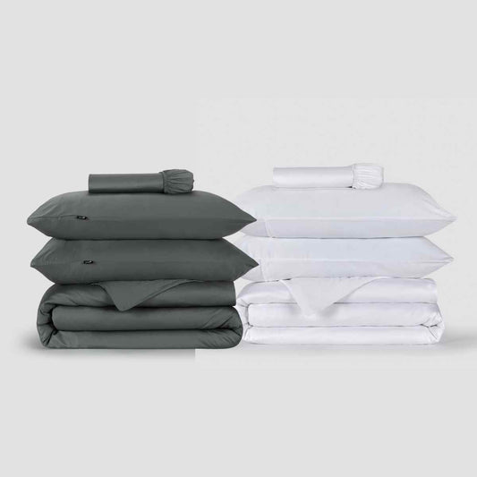 Dois conjuntos de capas de edredão Momo Cotton apresentados lado a lado, um cinzento e outro branco, empilhados com almofadas