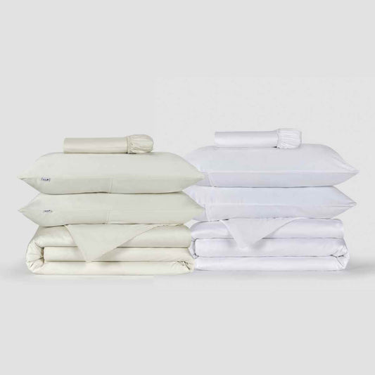 Conjuntos de roupa de cama creme e branco com capas de edredão, almofadas e lençóis dobrados sobre fundo branco