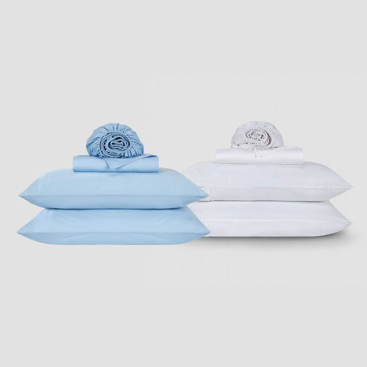 Jogo de lençol azul e branco em algodão exibido com almofadas e roupa de cama enrolada em fundo neutro