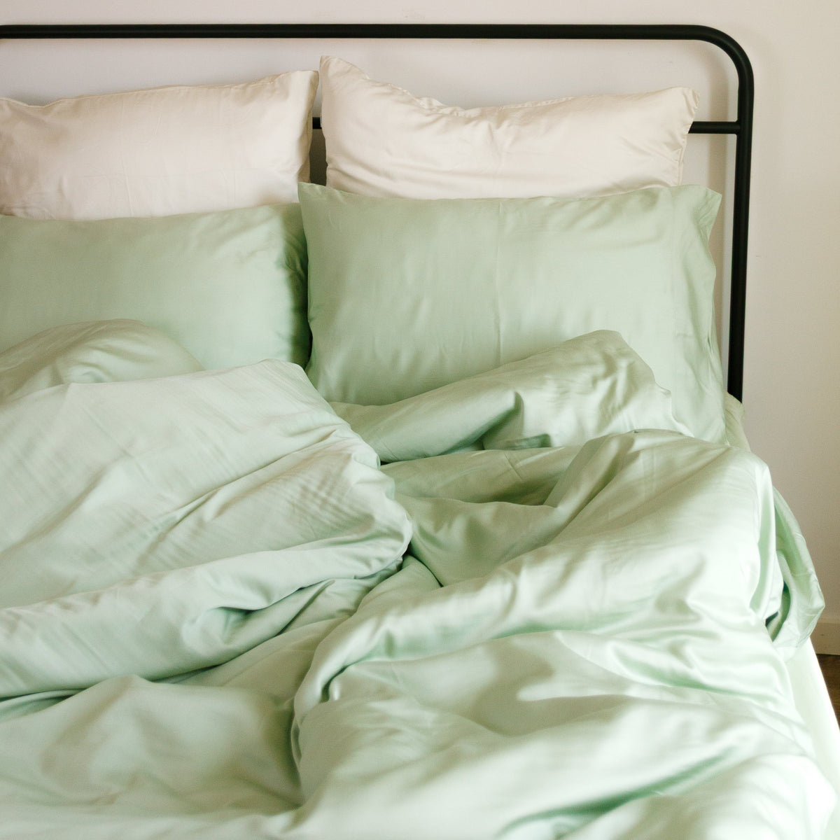Light green and white duvet cover set on bed with black frame, decorative rattan plates on wall