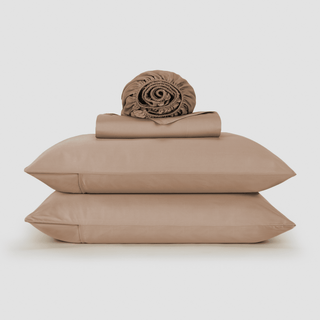 Conjunto de lençol de bambu bege empilhado com colcha enrolada e duas almofadas em fundo branco