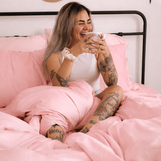Mulher deitada confortavelmente em lençol de bambu rosa, enfatizando a textura sedosa e o drapeado suave.